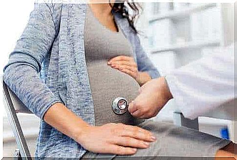 A doctor places a stethoscope on a pregnant woman's abdomen.