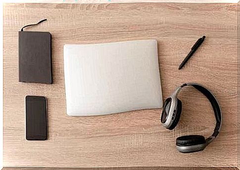 A planner, a smartphone, a laptop, a pen and headphones neatly arranged on a desk.