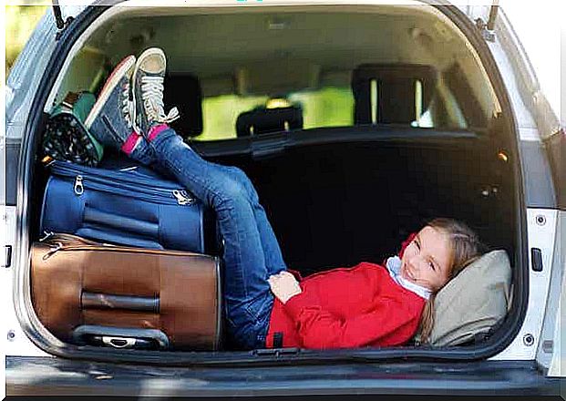 A child resting in the back of a parked car with his legs on the suitcases